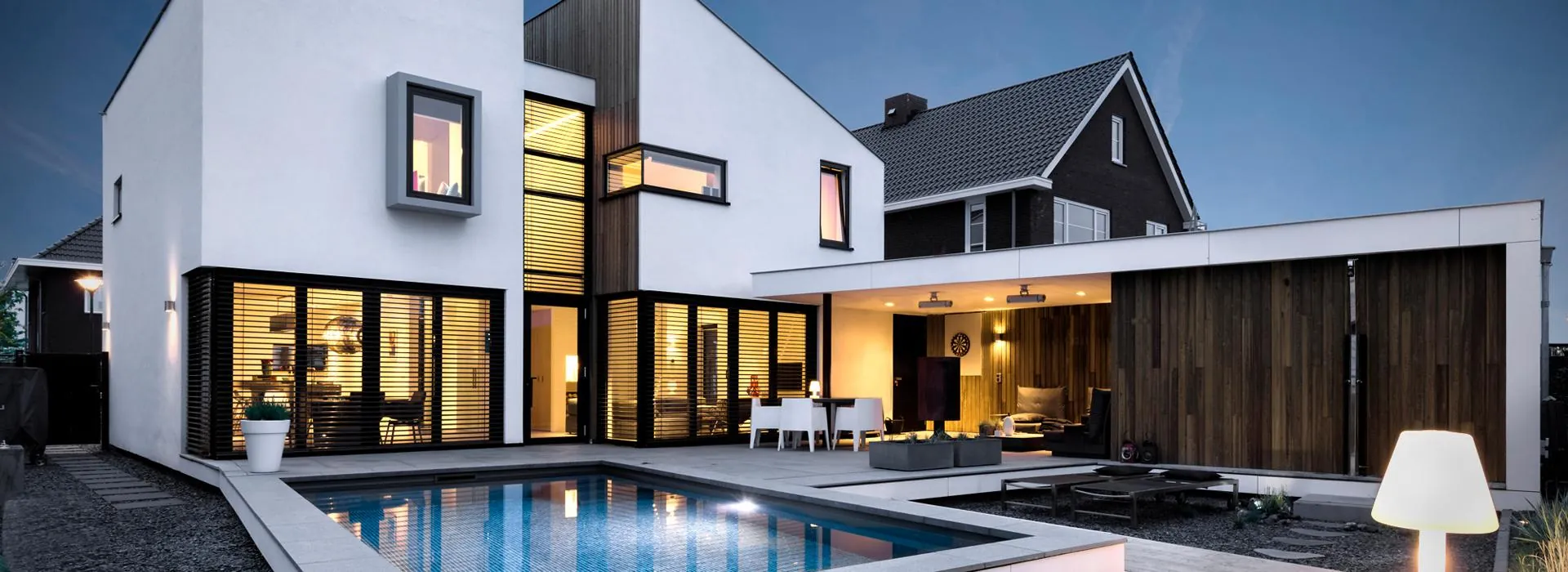 Modernes weißes Wohnhaus in der Abenddämmerung mit großen Glasflächen, Raffstoren und Pool
